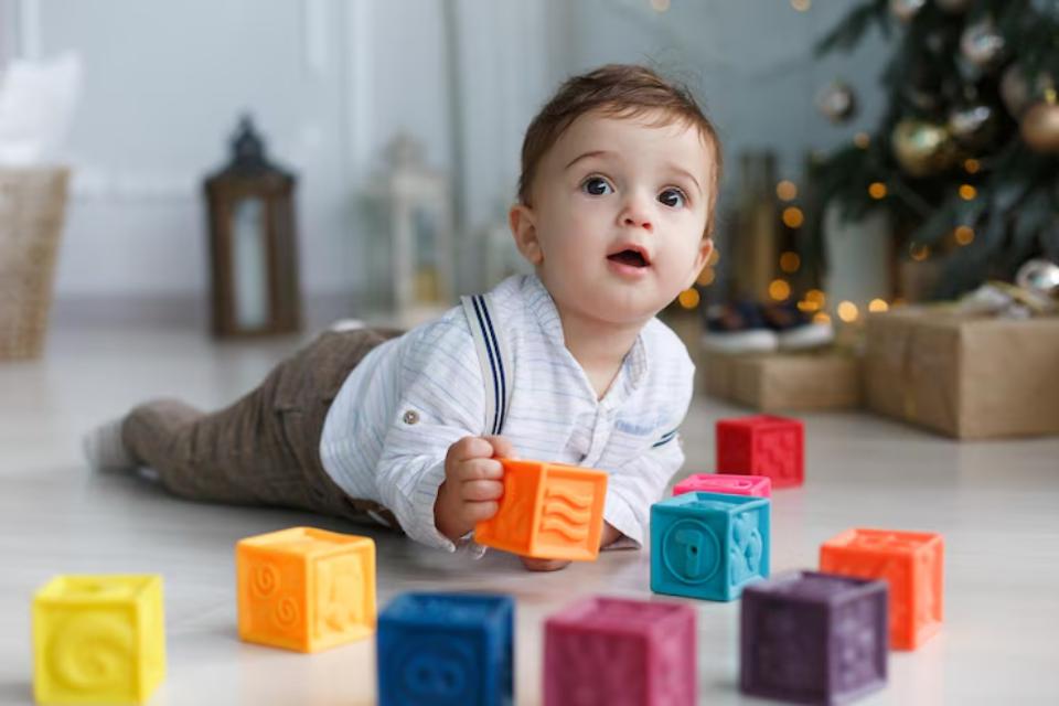  A young child lies on the floor playing with colorful building blocks, surrounded by a festive holiday atmosphere.