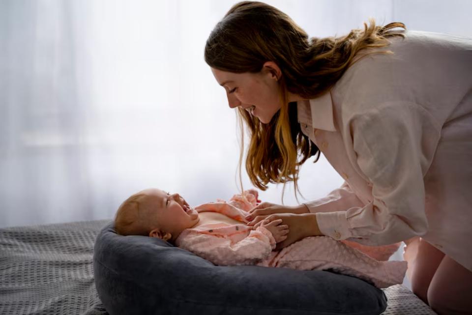  A woman in a light shirt gently interacts with a baby in a cozy seating area, surrounded by soft, natural light.