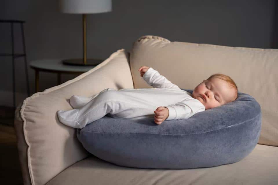A cozy, round blue pillow supports a baby lying on a light beige couch, creating a serene and comfortable atmosphere.