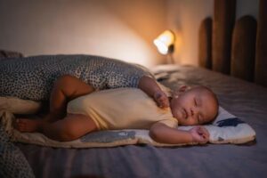 A peaceful baby lies asleep on a cozy bed, surrounded by soft bedding and warm light, creating a serene atmosphere.