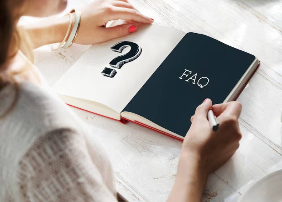 A person holds a notebook open to a page marked FAQ, with a hand drawing a question mark above it.