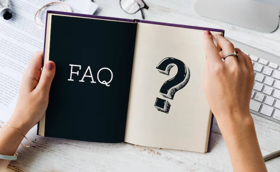 A person holding an open book displaying FAQ and a large question mark on the right page, surrounded by office supplies.