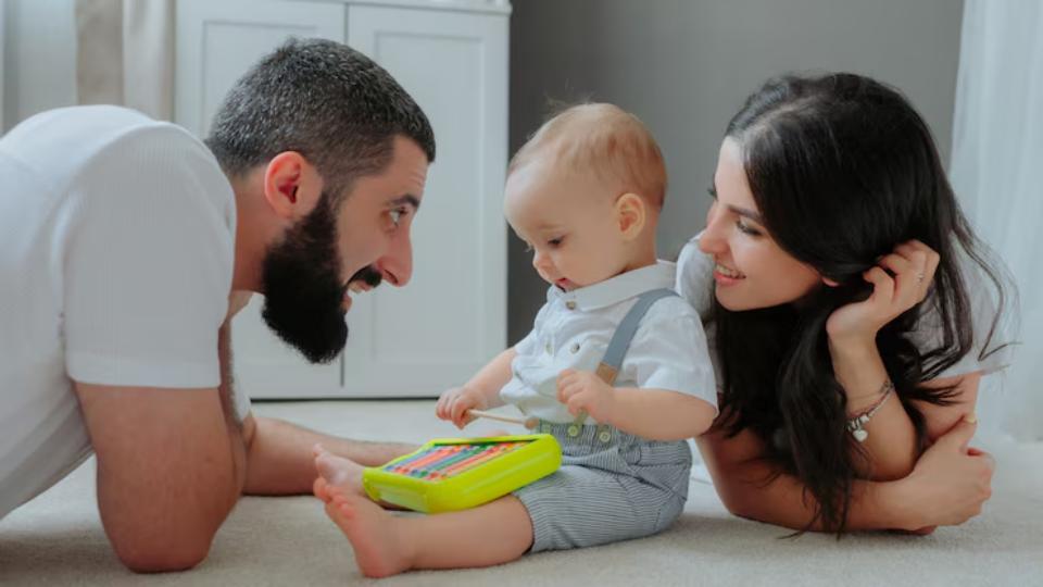  A baby sits on a soft carpet, playing with a colorful xylophone, while two adults watch closely, enjoying the moment together.