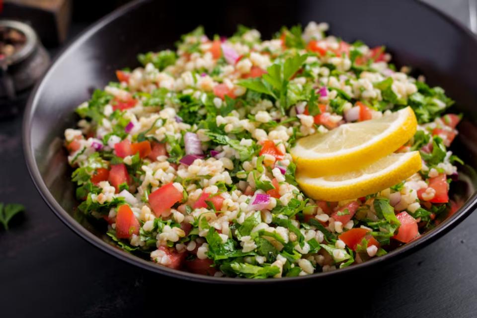  A vibrant bowl of tabbouleh salad with parsley, tomatoes, bulgur, and red onion, garnished with lemon slices.