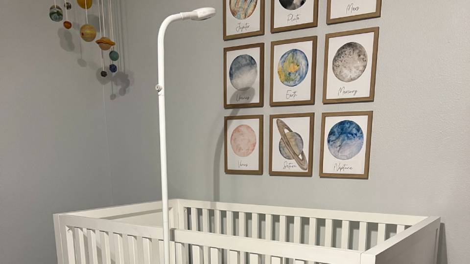 A cozy nursery featuring a white crib, a mobile with planets, and framed watercolor planetary art on the wall above.