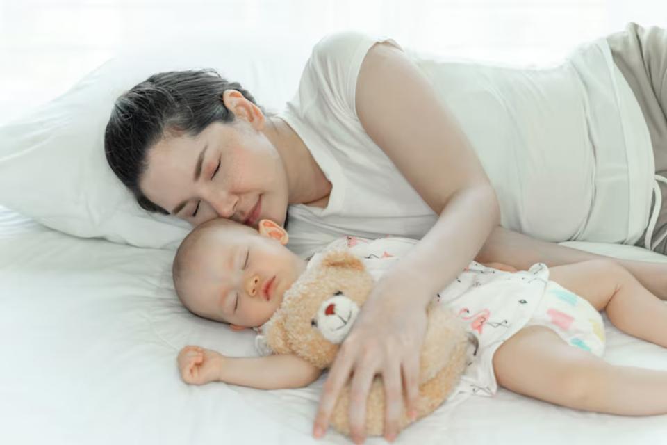  A calm scene of a woman lying on a bed, peacefully cradling a baby holding a teddy bear, bathed in soft natural light.