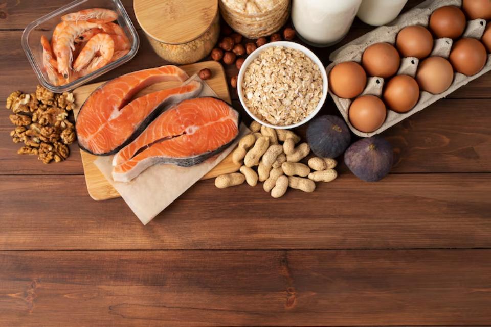  An assortment of fresh foods: salmon fillets, shrimp, eggs, oats, milk, nuts, and figs, arranged on a wooden table.