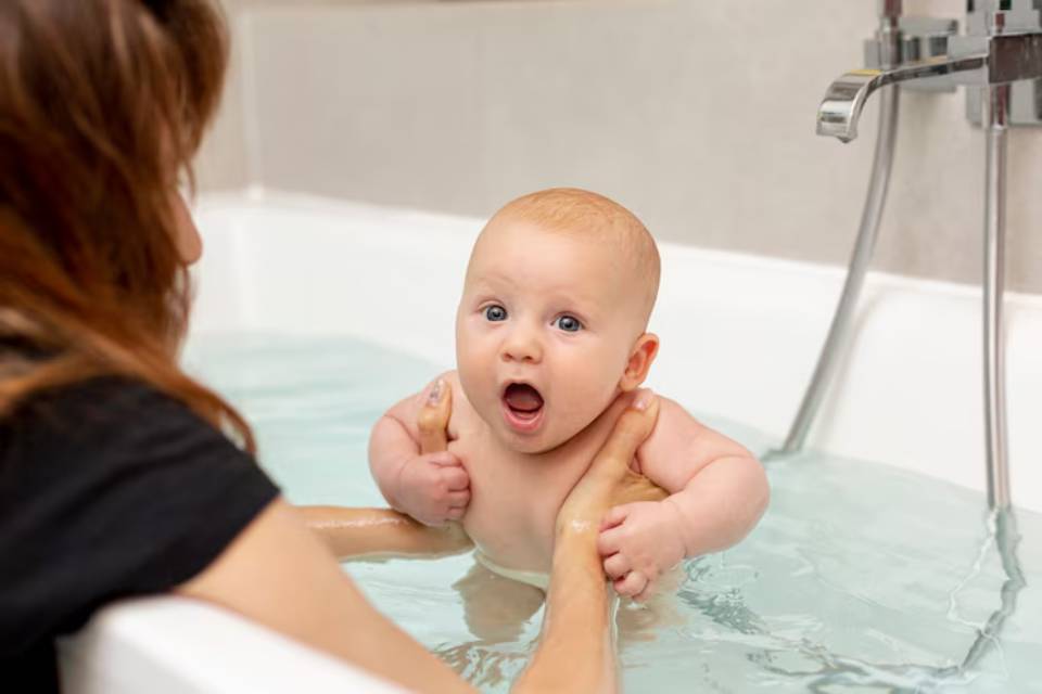 A caregiver gently holds a baby in a shallow bath, surrounded by warm water, creating a serene and nurturing atmosphere.