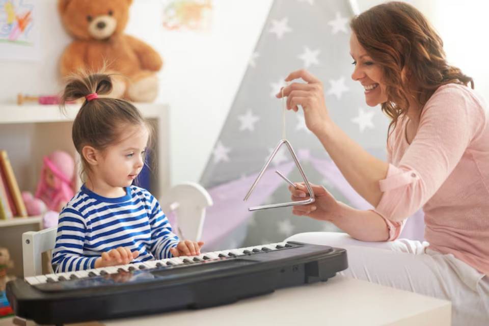 A child plays a keyboard while an adult demonstrates how to play a triangle, surrounded by a cozy, playful environment.