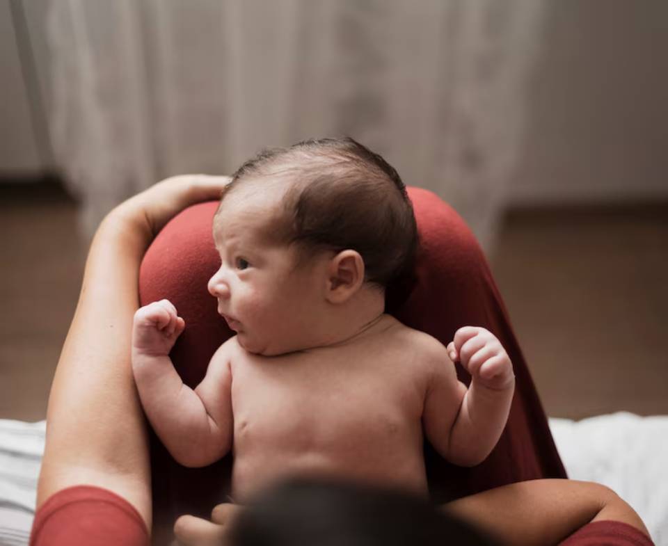 A baby in a cozy setting, nestled in a person's lap, with tiny fists raised in excitement, surrounded by soft textures and gentle lighting.