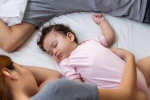 A peaceful family scene on a bed, with a baby in a pink onesie resting between two adults, showcasing affection and togetherness.