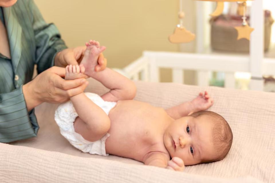  A caregiver gently plays with a baby's feet during a diaper change in a cozy nursery, with a crib and mobile in the background.