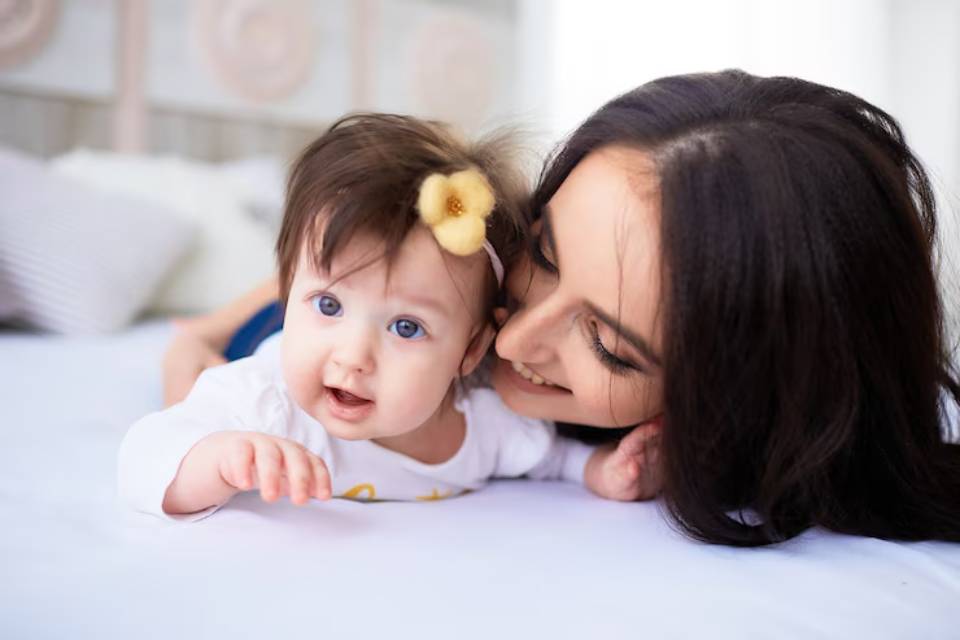A joyful moment captured of a baby reaching out playfully while lying on a soft bed, with cozy pillows in the background.