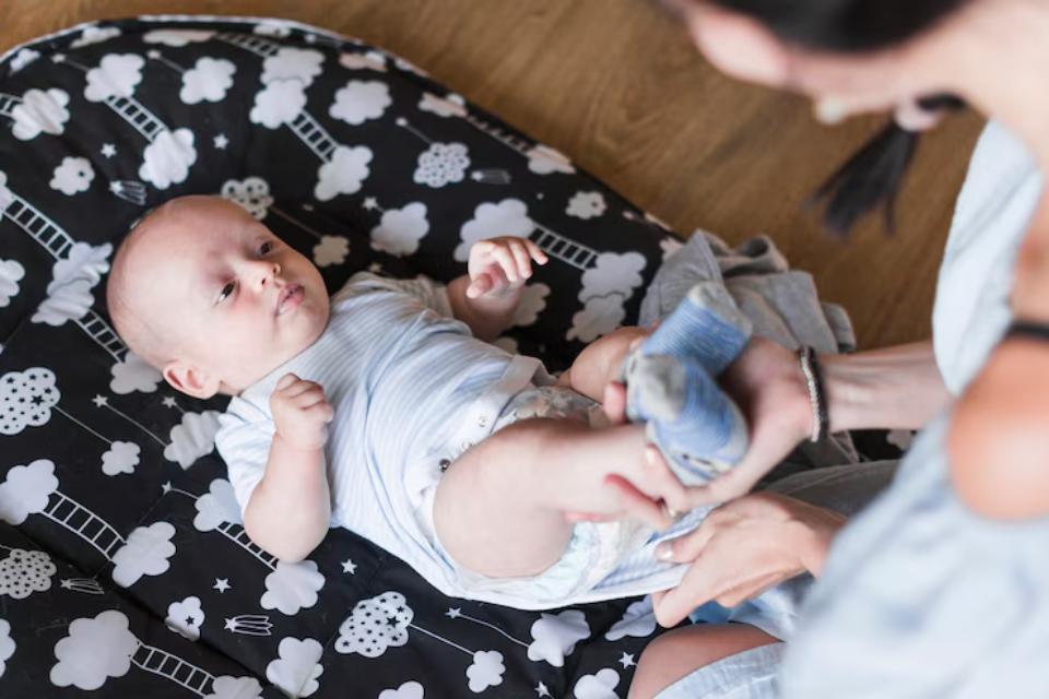  A caregiver gently dressing a baby on a black and white cloud-patterned blanket, surrounded by soft textures and warm lighting.