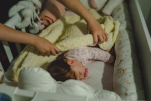 A woman gently holds the hand of a sleeping baby in a crib, creating a serene and nurturing atmosphere.