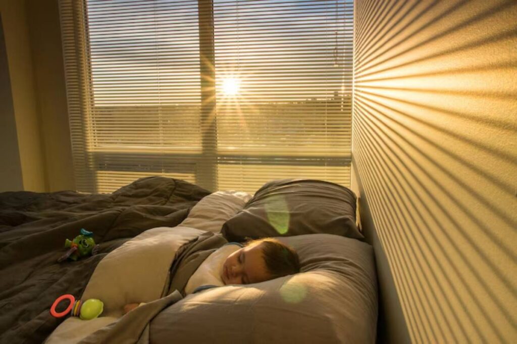 A cozy bedroom scene with golden sunlight streaming through blinds onto a bed, highlighting colorful toys scattered on the sheets.