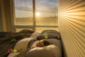 A cozy bedroom scene with golden sunlight streaming through blinds onto a bed, highlighting colorful toys scattered on the sheets.