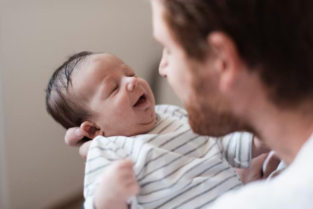 A parent gently holds a baby dressed in a striped outfit, smiling affectionately in a cozy indoor setting.