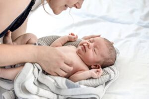 A close-up of a mother interacting lovingly with her wrapped baby on a soft, neutral-toned blanket, showcasing a tender moment.